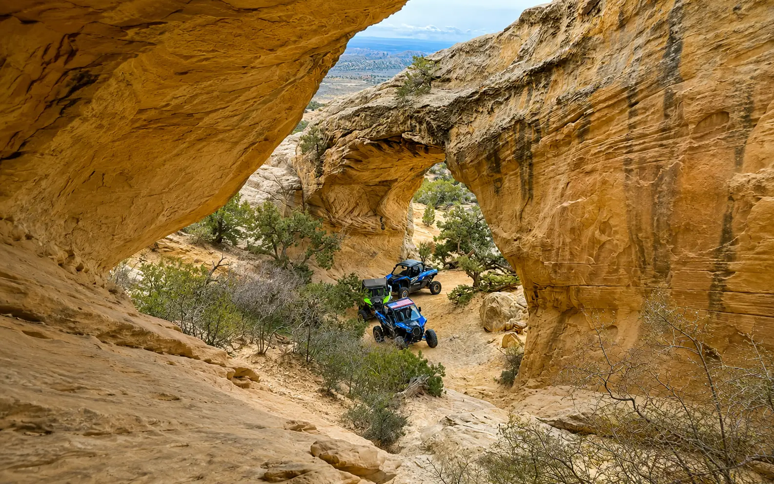 Two side-by-side UTVs on the backcountry trail beneath Moonshine Arch near Vernal, Utah